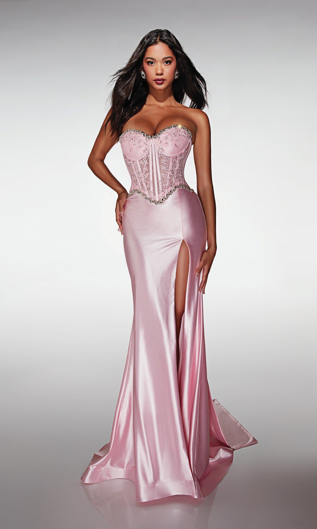 A woman stands against a plain background wearing the Alyce 62089 long prom dress, featuring a strapless fitted lace corset bodice, beaded details, and a high-leg slit.